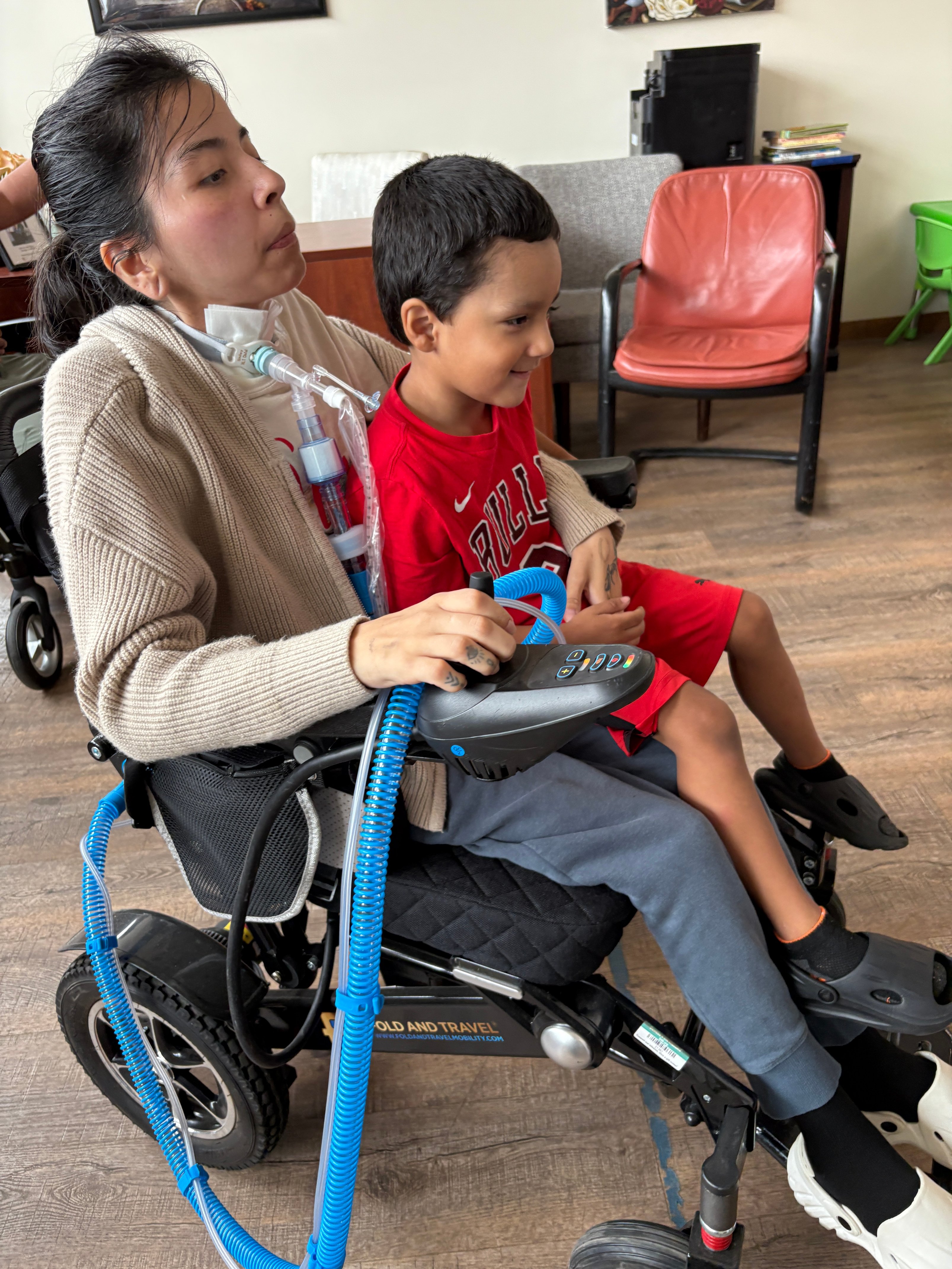 Profile of Maria in her new wheelchair with her 4-year-old son on her lap