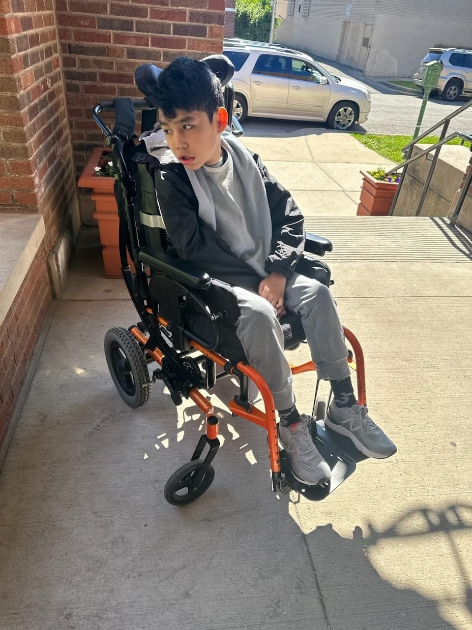 boy sitting outside in a wheelchair on a sunny day in the shade of his front porch