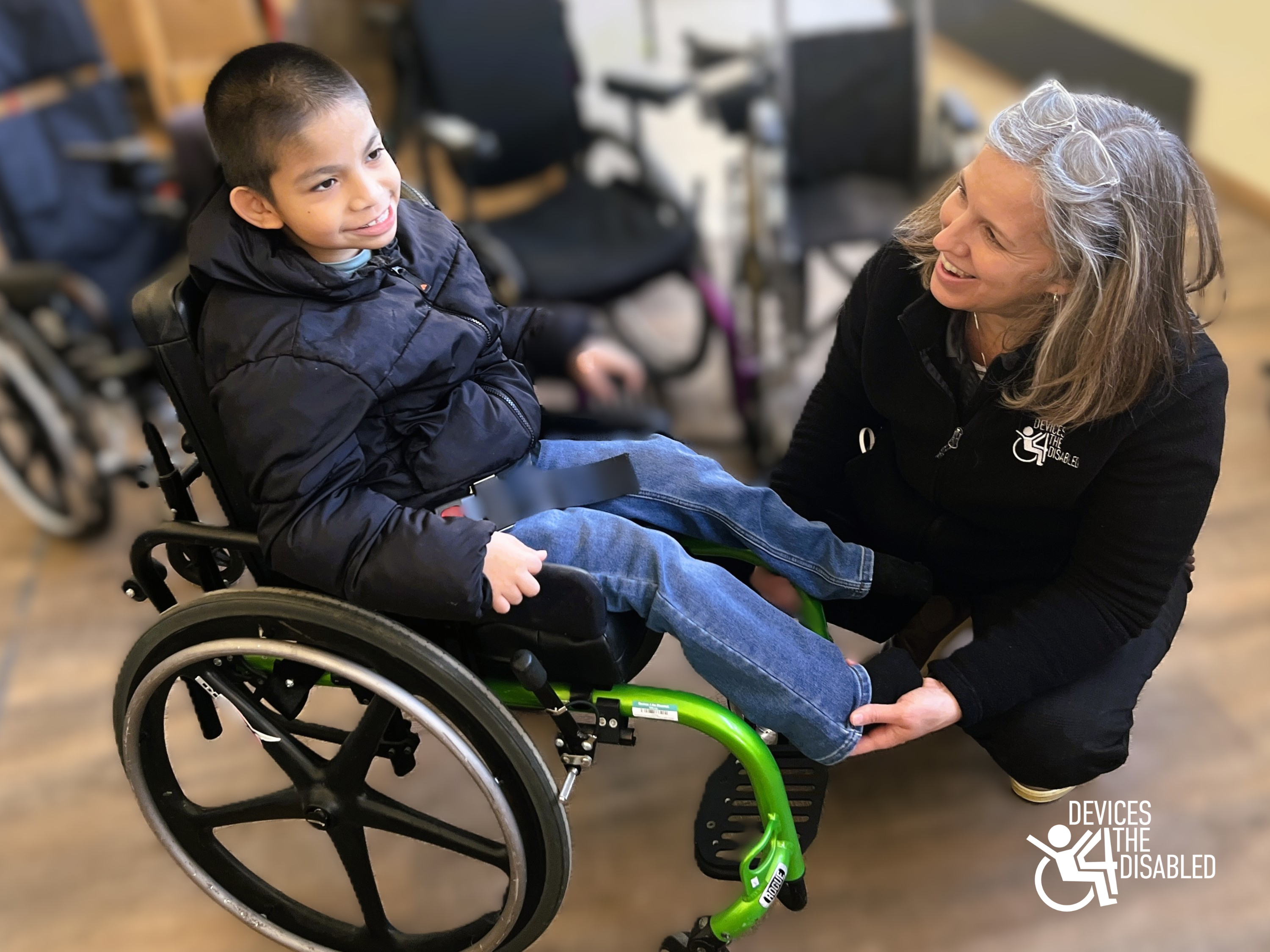 Jacob sitting in a wheelchair while a woman positioned low next to him helps fit the wheelchair.